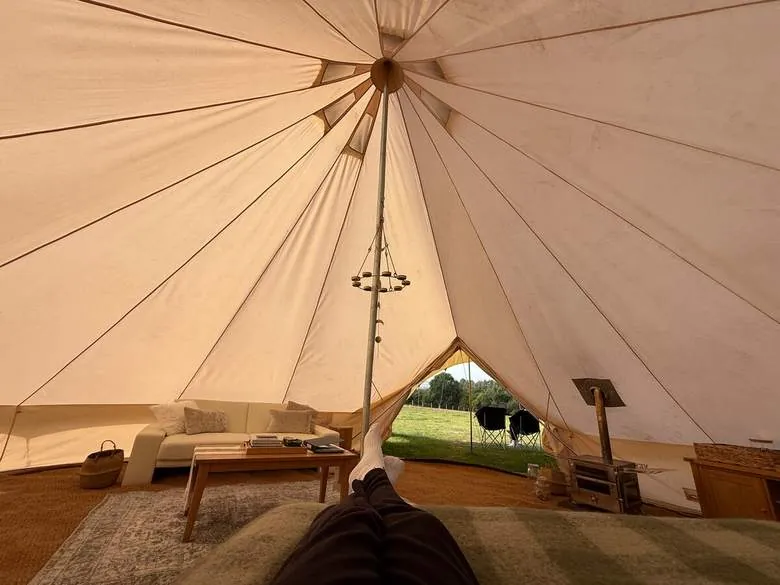 Inside a furnished bell tent with a sofa, wood burner and a view out to the field