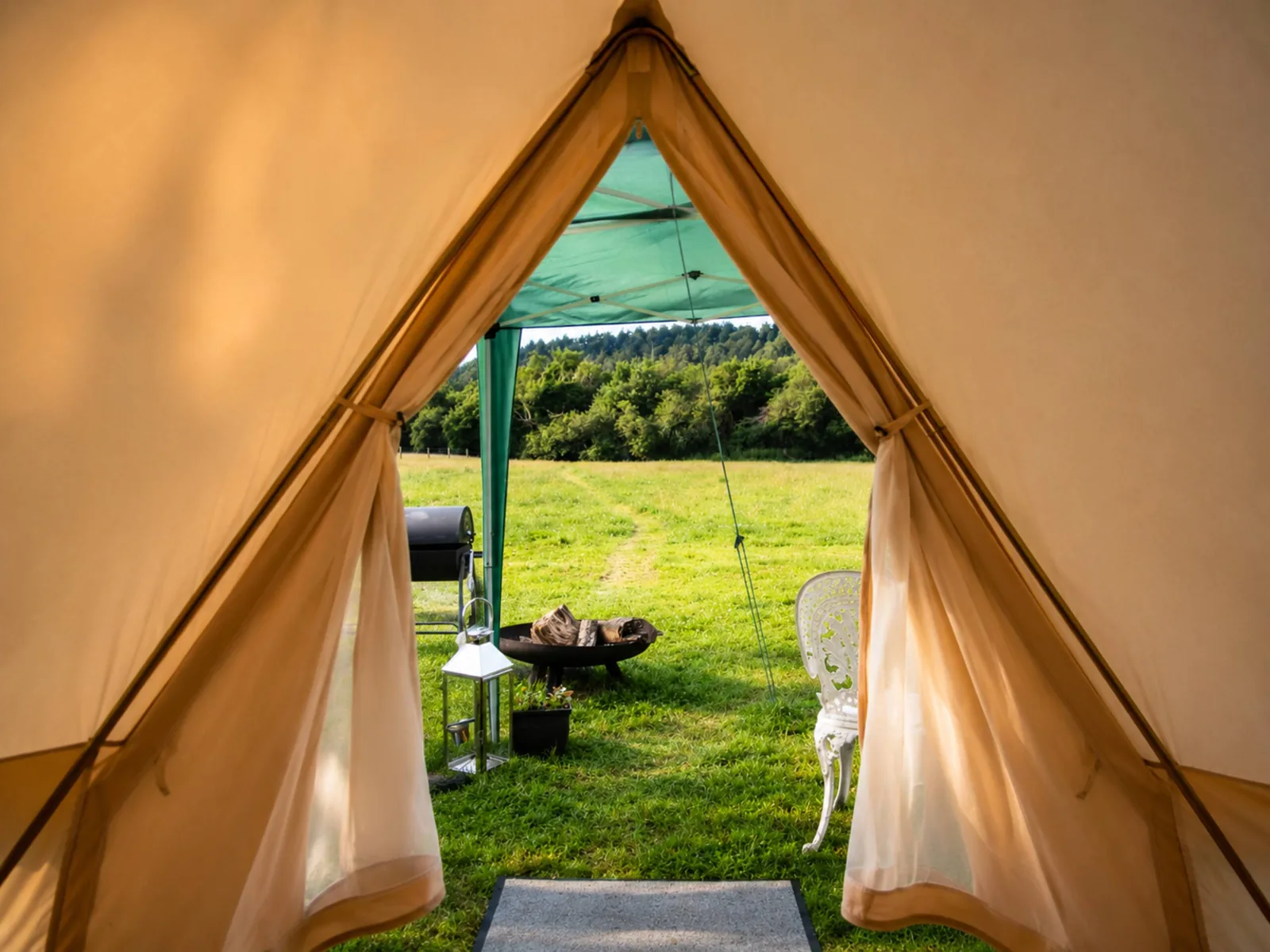 Looking out through the open tent doorway to the fire pit and chairs on the field