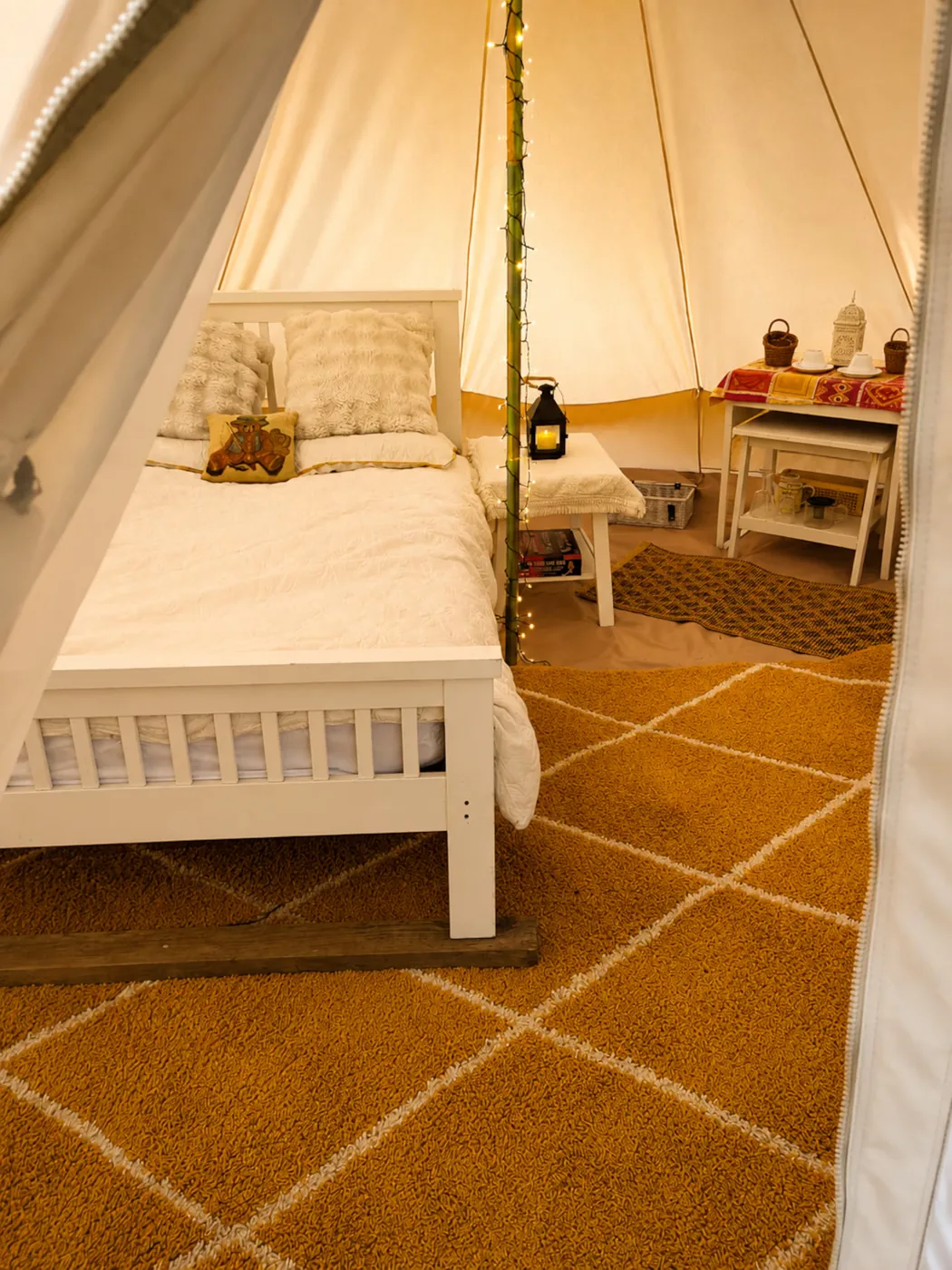The Bell Tent interior in soft morning light, bed made up beside a woven rug