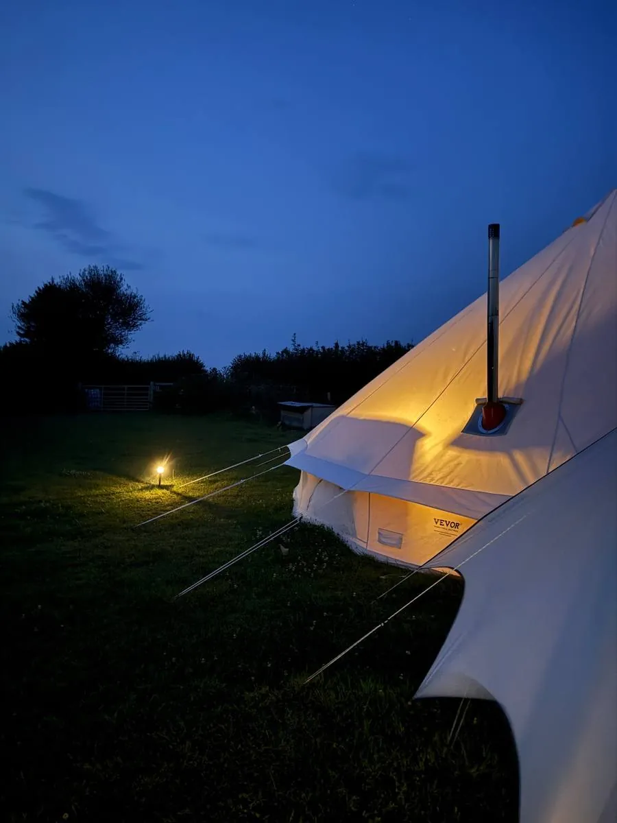 A lit bell tent under a pitch-black night sky