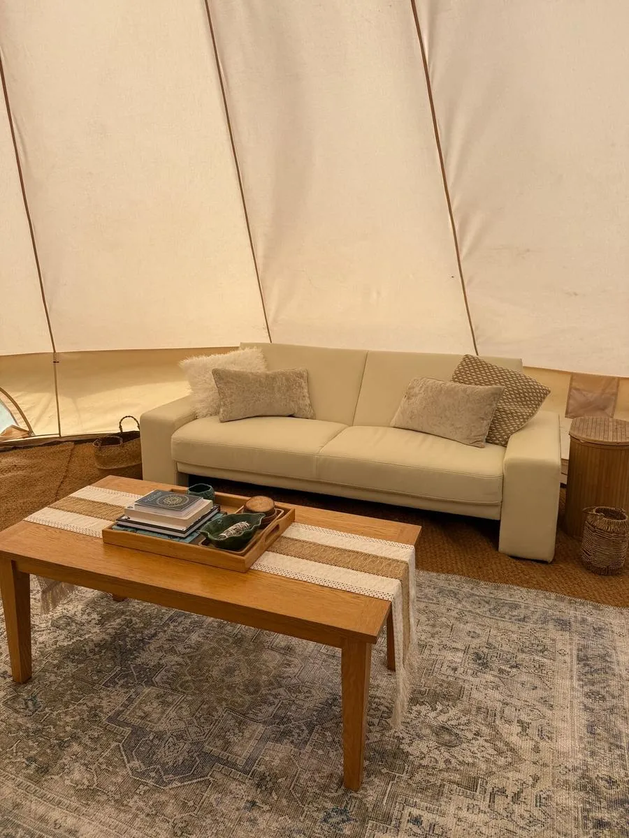 Inside a bell tent: a made-up bed with linen, blankets and a bee cushion
