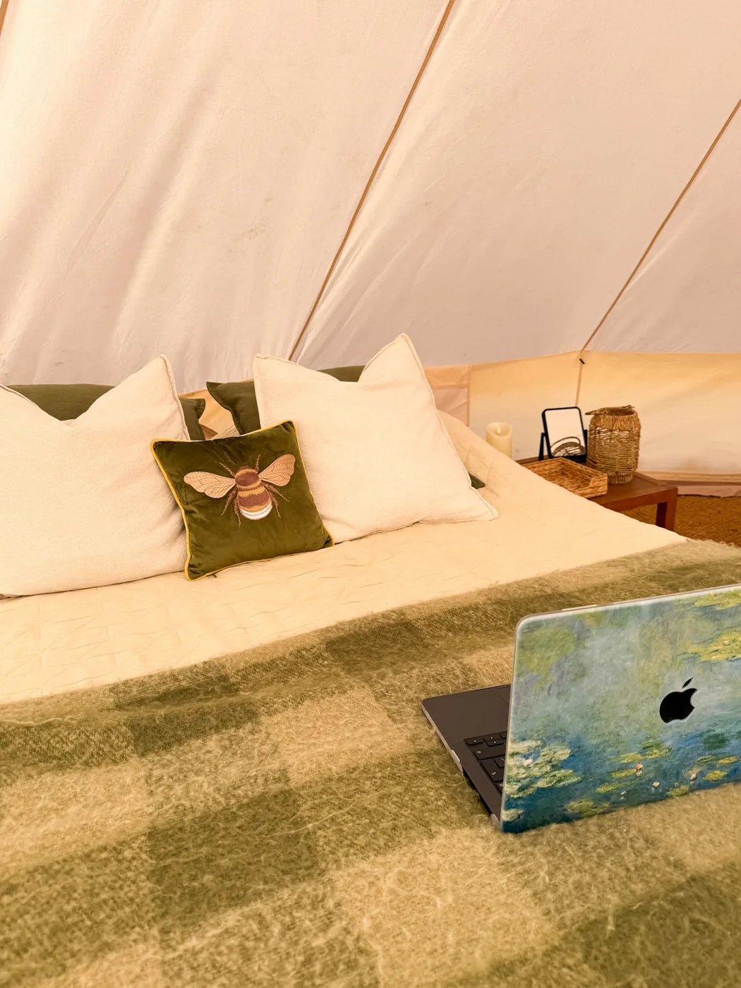 A made-up double bed in the Family Tent with a bee cushion and check blanket